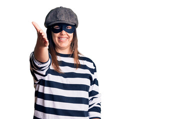 Young beautiful brunette woman wearing burglar mask smiling friendly offering handshake as greeting and welcoming. successful business.
