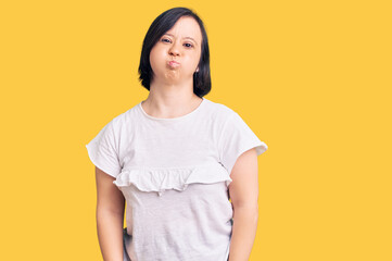 Brunette woman with down syndrome wearing casual white tshirt puffing cheeks with funny face. mouth inflated with air, crazy expression.