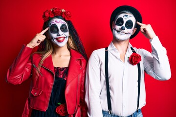 Couple wearing day of the dead costume over red smiling pointing to head with one finger, great idea or thought, good memory