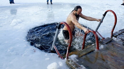 Holy Epiphany. Christian Baptism. Orthodox Epiphany. Swimming in the icy hole. A man emerges from the icy water in a icy hole in the winter in Ukraine