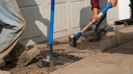 breaking up an asphalt driveway with a sledgehammer and a pickax 