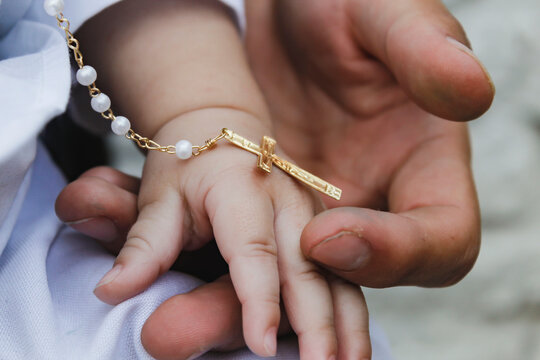 Man's hand holding the hand of a baby, on the day of his christening and with a medal of the cross. - Powered by Adobe