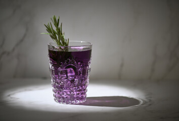 Closeup shot of a glass of purple drink with rosemary leaves