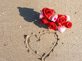 Romantic Red Rose Laying on a Heart Drawn in Beach Sand