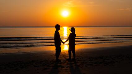 Romantic couple on the beach at colorful sunset on background.