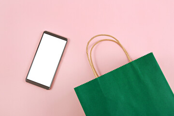 Top view of shopping bag and smartphone with blank screen on pastel pink background.