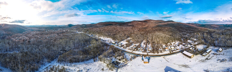 winter aerial drone panorama - a small village of Tkhamaha in the mountains of the Western Caucasus (South Russia), swept by snow, surrounded by forest, on a sunny day