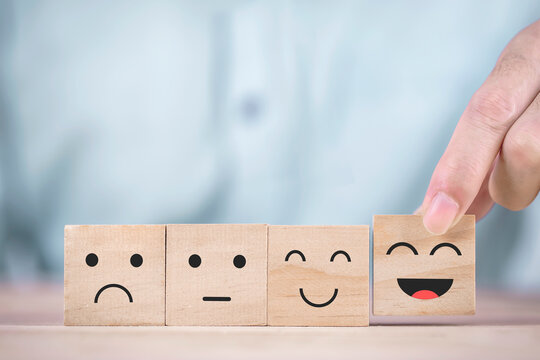 Businessman chooses a smiley face happy symbol on wooden block , Services and Customer satisfaction survey concept