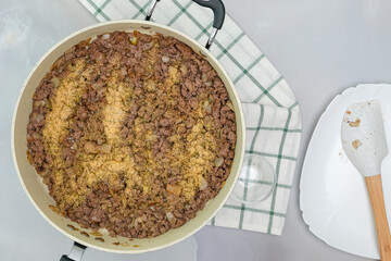 Ground beef, chopped onion, and garlic seasoning close up on frying pan, flat lay
