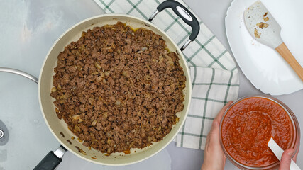 Ground meat fried with chopped onion, black pepper, and garlic seasoning close up on frying pan, and marinara sauce in a bowl.  Beef lasagna step by step recipe