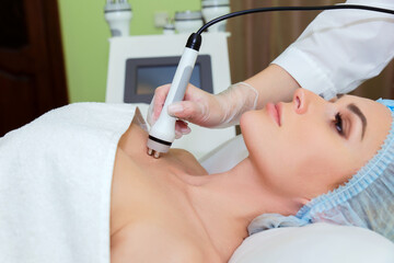 The spa salon's cosmetologist performs a RF lifting procedure on the neckline of a young woman.
