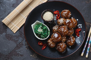 Black plate with asian-style teriyaki sauce meatballs, high angle view on a brown stone background, studio shot