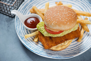 Blue and white plate with fishburger, french fries and dipping sauce, studio shot on a grey concrete background