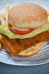 Close-up of burger with sesame bun, fish cutlet, vegetables and sauce, vertical shot, selective focus