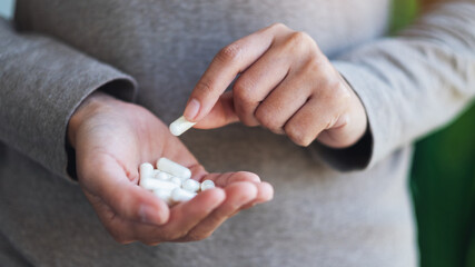 Closeup image of a woman holding and picking white medicine capsules in hand