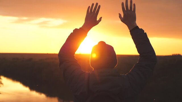 Silhouette of a man at sunset with raised hands against the sunset. A man dreams of floating in the air with open arms. Dream and pray looking to the sky