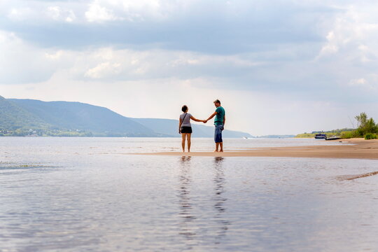 a beautiful mature couple walks along the wild beach holding hands against the background of the Volga open spaces and the Zhiguli mountains on a summer day
