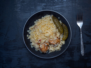 Lunch with rice, chicken drumstick and pickled cucumbers on a black plate