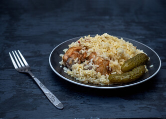 Rice and chicken drumsticks with pickled cucumbers on a black plate and a fork