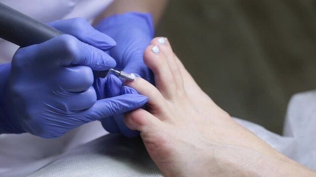 The nail technician removes the gel coat from the toenails. Hardware pedicure in the salon.