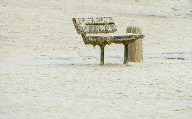 Fototapeta na wymiar bench at the coast covered with sea foam or spume during a coastal storm in Winter concept weather and climate change