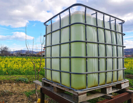 Plastic water tank in a farm field under a blue cloudy sky and sunlight