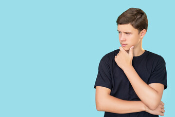 Pensive guy. Commercial background. Interesting opportunity. Portrait of puzzled curious confused teen boy in black t-shirt considering option looking at invisible text isolated on blue copy space. - obrazy, fototapety, plakaty