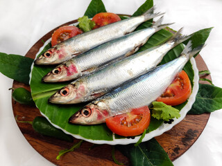 Fresh Slender Rainbow Sardine decorated with vegetables and herbs on a wooden pad.Selective Focus.