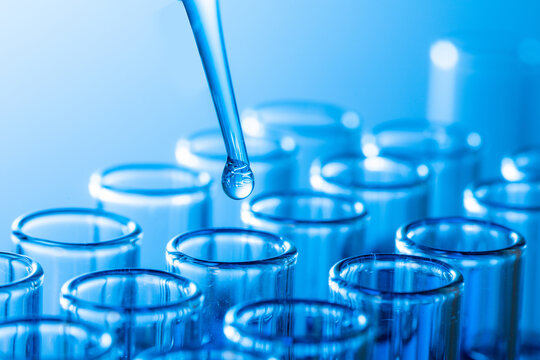 Closeup Shot Of A Pipette Tip With A Droplet Over Glass Test Tubes