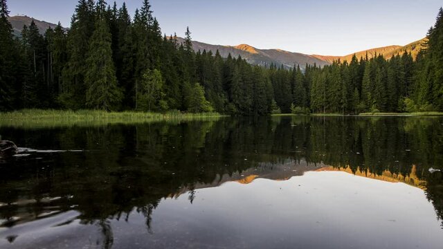 4K Time Lapse of Beautiful landscape with mountains illuminated, reflection in mountain lake, blue sky and yellow sunlight. Slovakia, Vrbicke Pleso Low Tatras