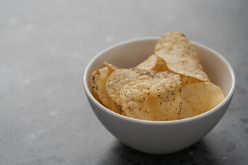White bowl with organic potato chips sprinkled with fresh ground black pepper on concrete background with copy space