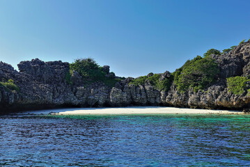 Fototapeta na wymiar A secluded beach on Koh Rok island in the Andaman Sea. A semicircular strip of sand is surrounded by rocks with green vegetation. The turquoise water is calm. Clear blue sky. Thailand