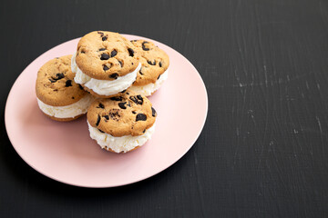 Homemade Chocolate Chip Cookie Ice Cream Sandwich on a pink plate on a black background, low angle view. Copy space.