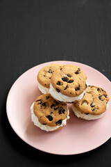 Homemade Chocolate Chip Cookie Ice Cream Sandwich on a pink plate on a black background, side view. Copy space.