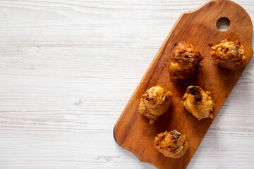 Homemade Spicy Chicken Lollipop on a rustic wooden board on a white wooden surface, top view. Overhead, from above, flat lay. Space for text.