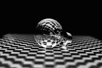 An abstract image of an incandescent lamp on a black-and-white checkered surface.