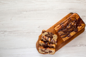 Homemade Chocolate Banana Bread on a rustic wooden board on a white wooden background, top view. Flat lay, overhead, from above. Copy space.