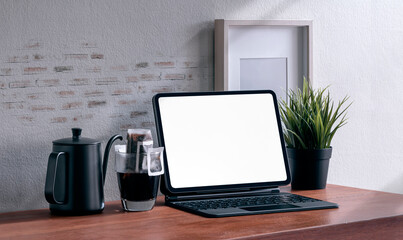 Mockup blank screen tablet with magic keyboard and drip coffee on wooden table.