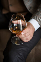 A man businessman holds a glass with alcohol in his hand. Dressed in a jacket and shirt. Rest after a working day
