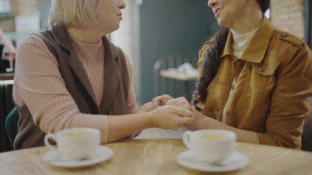 Two senior women holding hands, close friends talking in cafe, emotional support