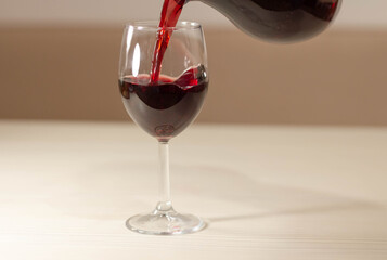 A glass of red wine is on the table. The wine flows into the glass like a stream