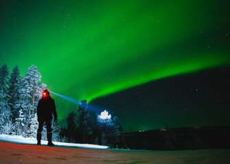 A traveler with a headlamp enjoys the view of the northern lights and space. High iso photo