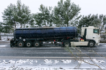 Fuel tanker parked in a freeway parking lot on a day complicated by the falling snow.