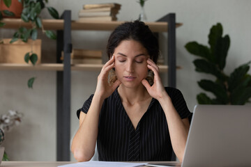 Tired young Caucasian woman work on laptop suffer from blurry vision or dizziness overwhelmed with screen job. Exhausted female use computer struggle with headache or migraine. Overwork concept.