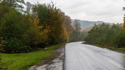 Autumn mountain landscape in the Ukrainian Carpathians - yellow and red trees combined with green needles. Deserted road in the mountains. High mountains in the background.