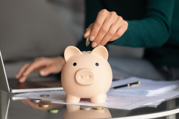 Close up of woman put drop coin into piggy bank managing budget paying bills taxes online on...