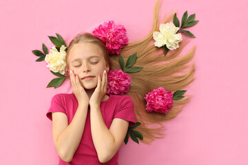 Obraz na płótnie Canvas A girl with peonies, beautiful blonde hair and a colorful children's manicure on a pink background.Fashion nail art and hairstyle.