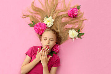 A girl with peonies, beautiful blonde hair and a colorful children's manicure on a pink background.Fashion nail art and hairstyle.