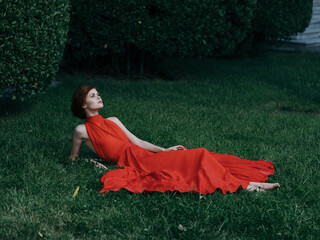 Attractive elegant woman outdoors lies on the grass red dress