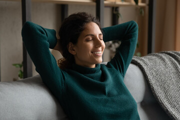 Smiling young Caucasian woman sit rest on sofa in living room with eyes closed sleeping or dreaming. Happy millennial female relax on couch at home relieve negative emotions. Stress free concept.